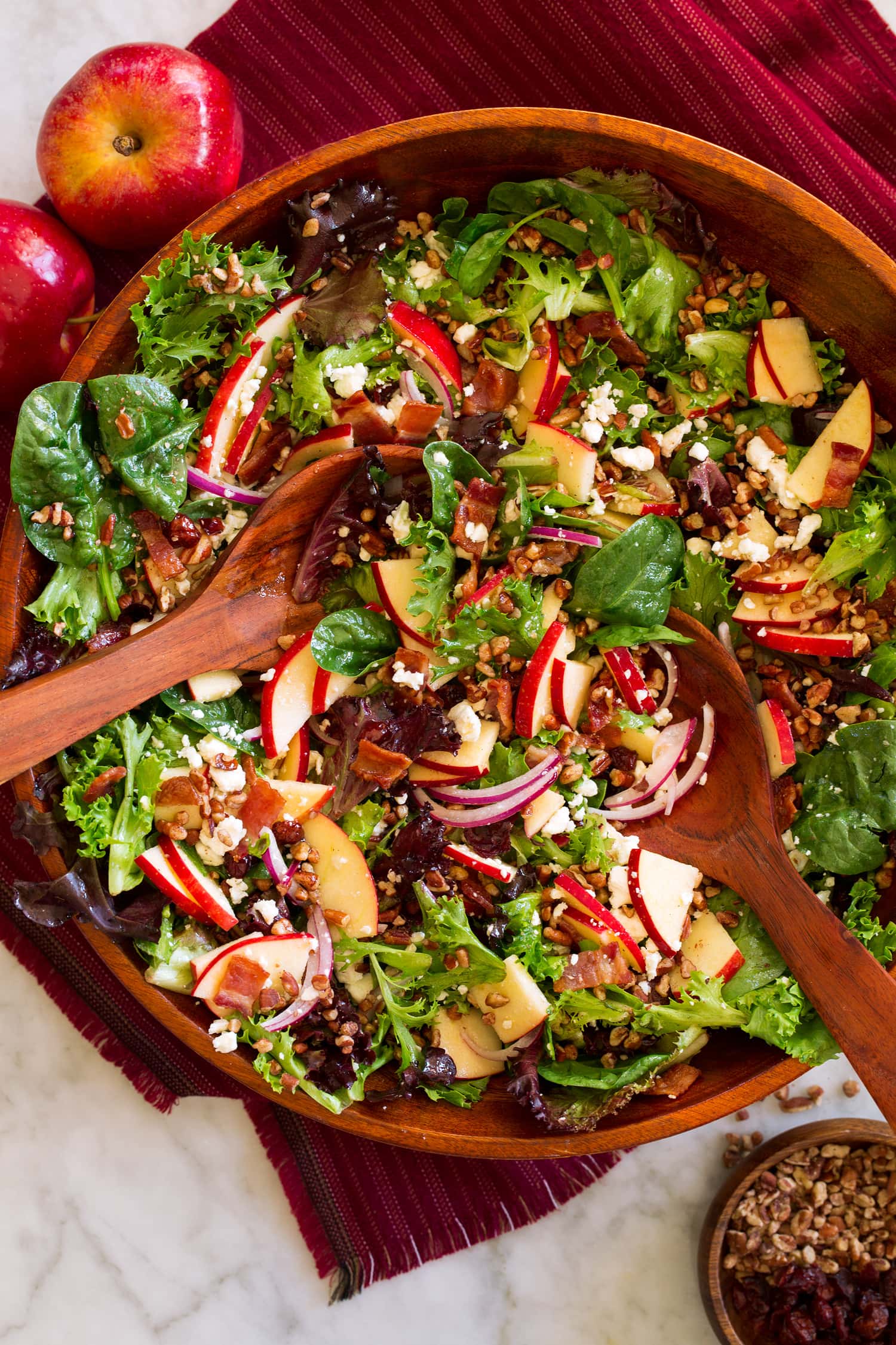 Overhead photo of apple salad in a wooden serving bowl with wooden serving spoons.
