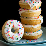 Image of stack of baked donuts on a plate. They are covered in icing and sprinkles.