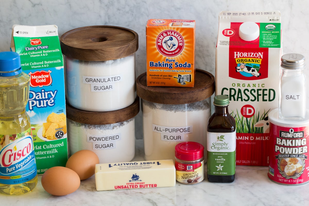 Photo of ingredients used to make baked donuts. Includes vegetable oil, buttermilk, eggs, butter, flour, powdered sugar, granulated sugar, nutmeg, vanilla extract, baking soda, baking powder, salt and milk.