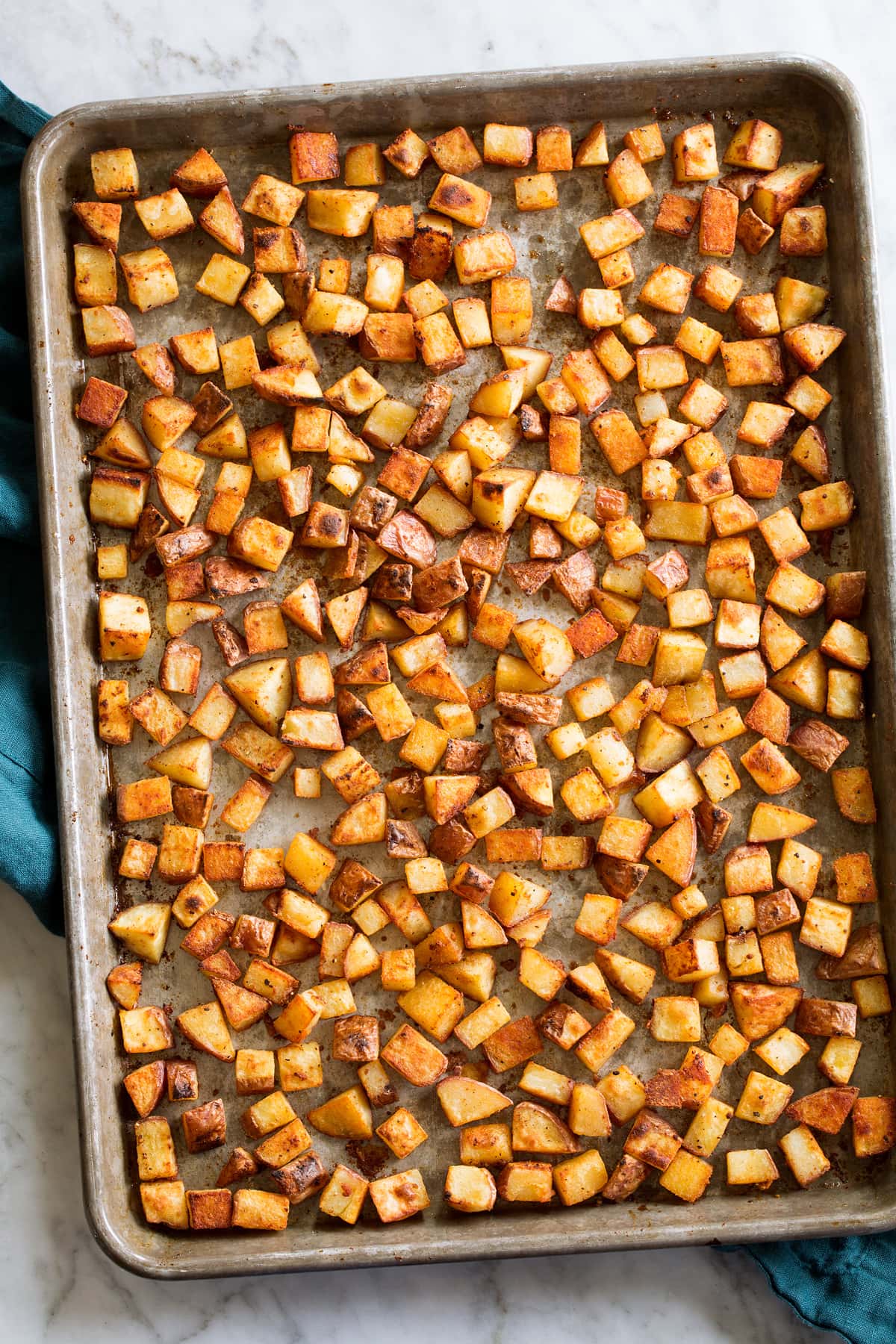 Photo: Crispy browned breakfast potatoes on a sheet pan set on a white marble surface.