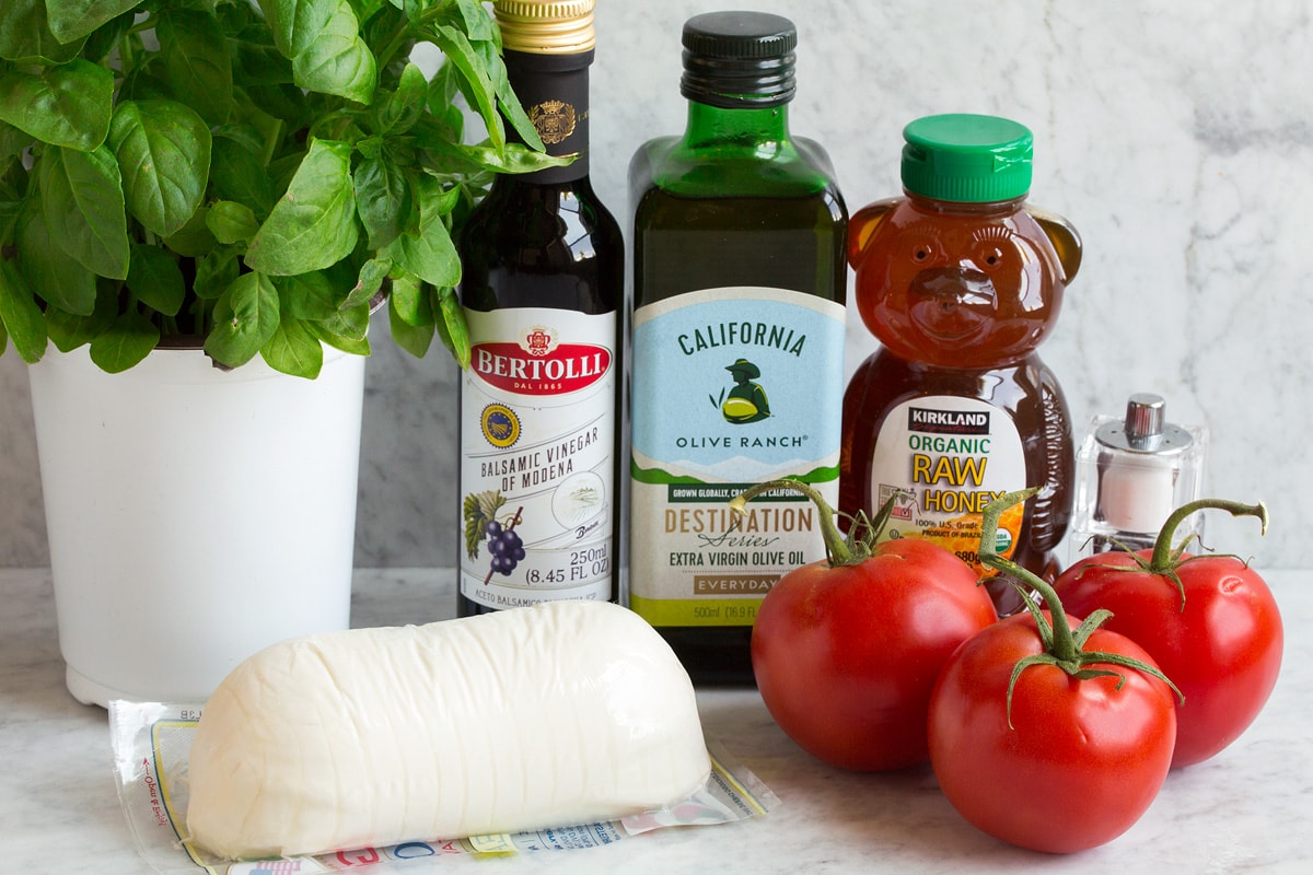 Caprese Salad Ingredients shown in this image. Includes fresh mozzarella, fresh basil, fresh tomatoes, olive oil, honey, balsamic vinegar, salt and pepper.