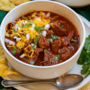 Chili con carne in a serving bowl topped with shredded cheese, cilantro and chopped onion.
