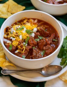 Chili con carne in a serving bowl topped with shredded cheese, cilantro and chopped onion.
