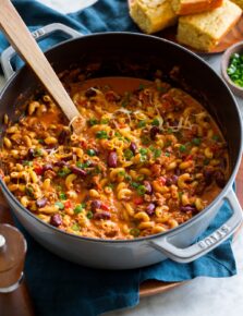 Chili mac in a large pot with a wooden spoon scooping mixture.