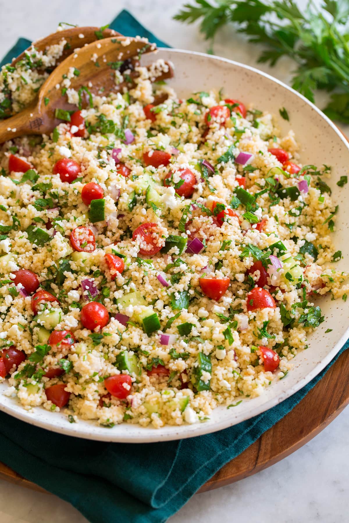 Couscous salad with cucumbers, tomatoes, and herbs shown in a white bowl from the side.