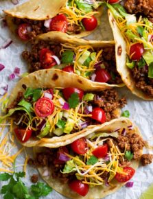 Row of ground beef tacos on parchment paper.