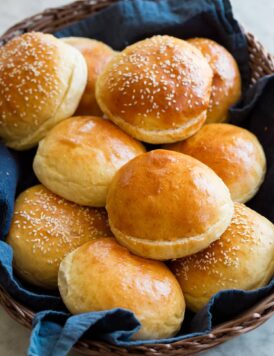 Homemade hamburger buns shown in a basket with a blue cloth.