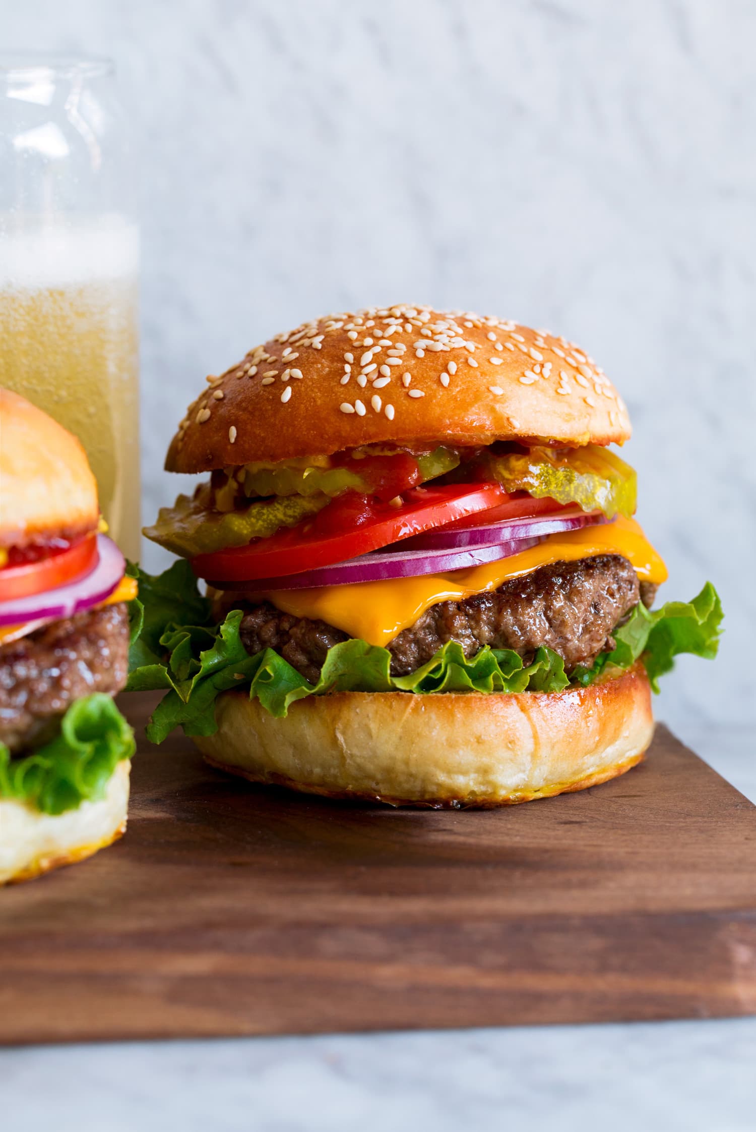 Hamburger shown on homemade bun with lettuce, cheddar, tomatoes and pickles.