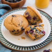 Healthy blueberry muffins on a white and blue plate with orange juice in the background.
