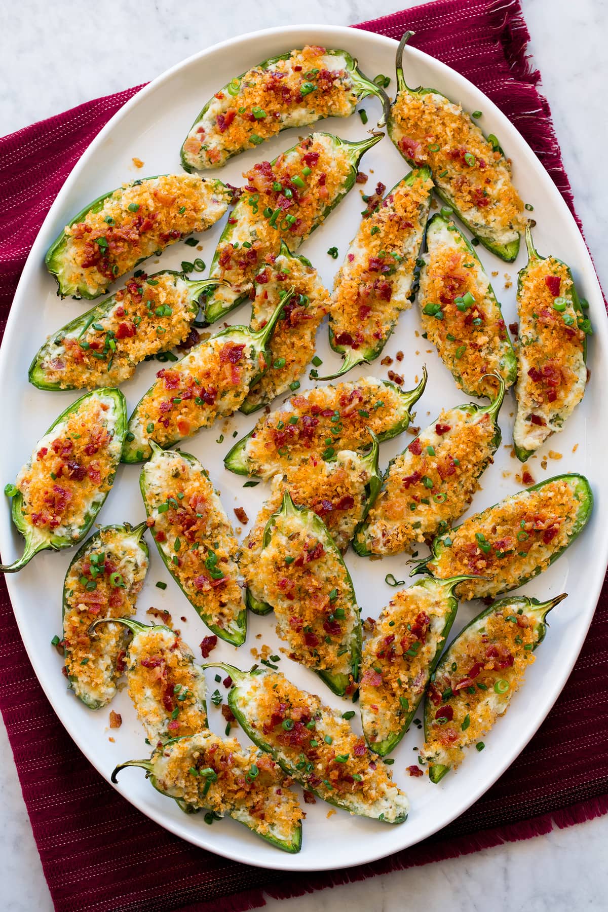 Overhead photo of jalapeno poppers on oval white platter over red cloth.
