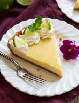 Slice of Best Key Lime Pie on white scalloped dessert plate set over a maroon napkin.