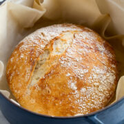 No knead bread in a large blue pot resting on parchment paper.