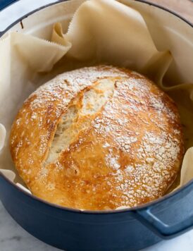 No knead bread in a large blue pot resting on parchment paper.