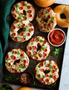 Bagel pizzas on a dark baking sheet.