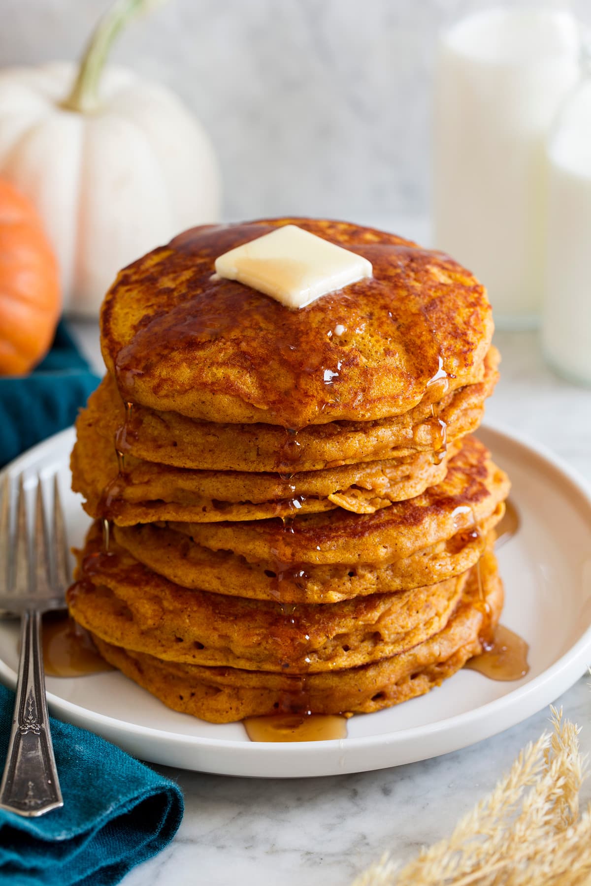 Stack of pumpkin pancakes on a platter. Pancakes are drizzled with maple syrup and topped with butter.