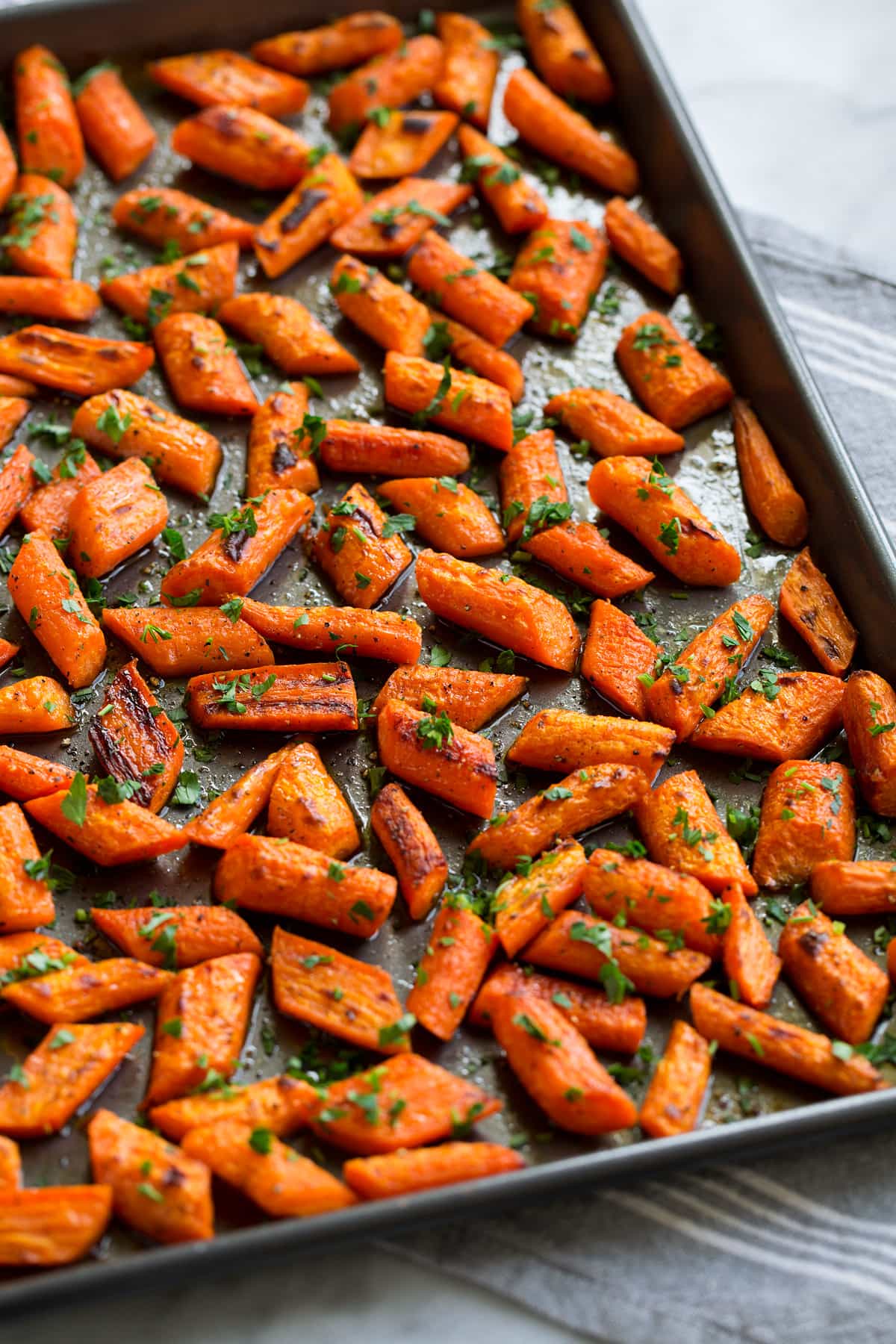 Photo: Roasted carrots shown from the side on a dark baking sheet.