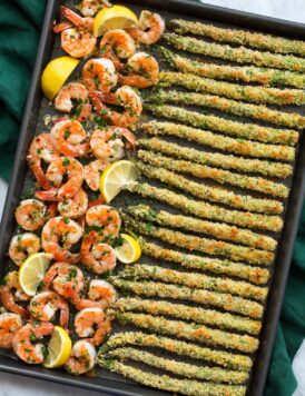 Photo of sheet pan filled with a row of garlic lemon butter shrimp on the left side and panko parmesan crusted asparagus on the ride side. Shown from overhead.