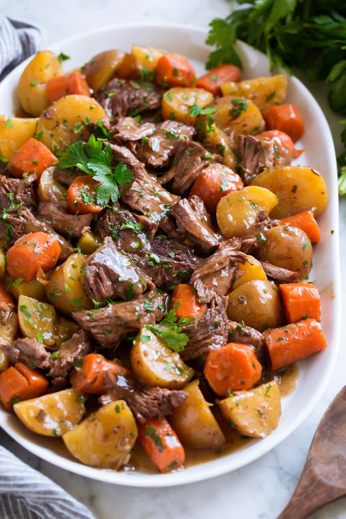 Shredded slow cooker pot roast with potatoes and carrots on a white serving platter garnished with parsley.