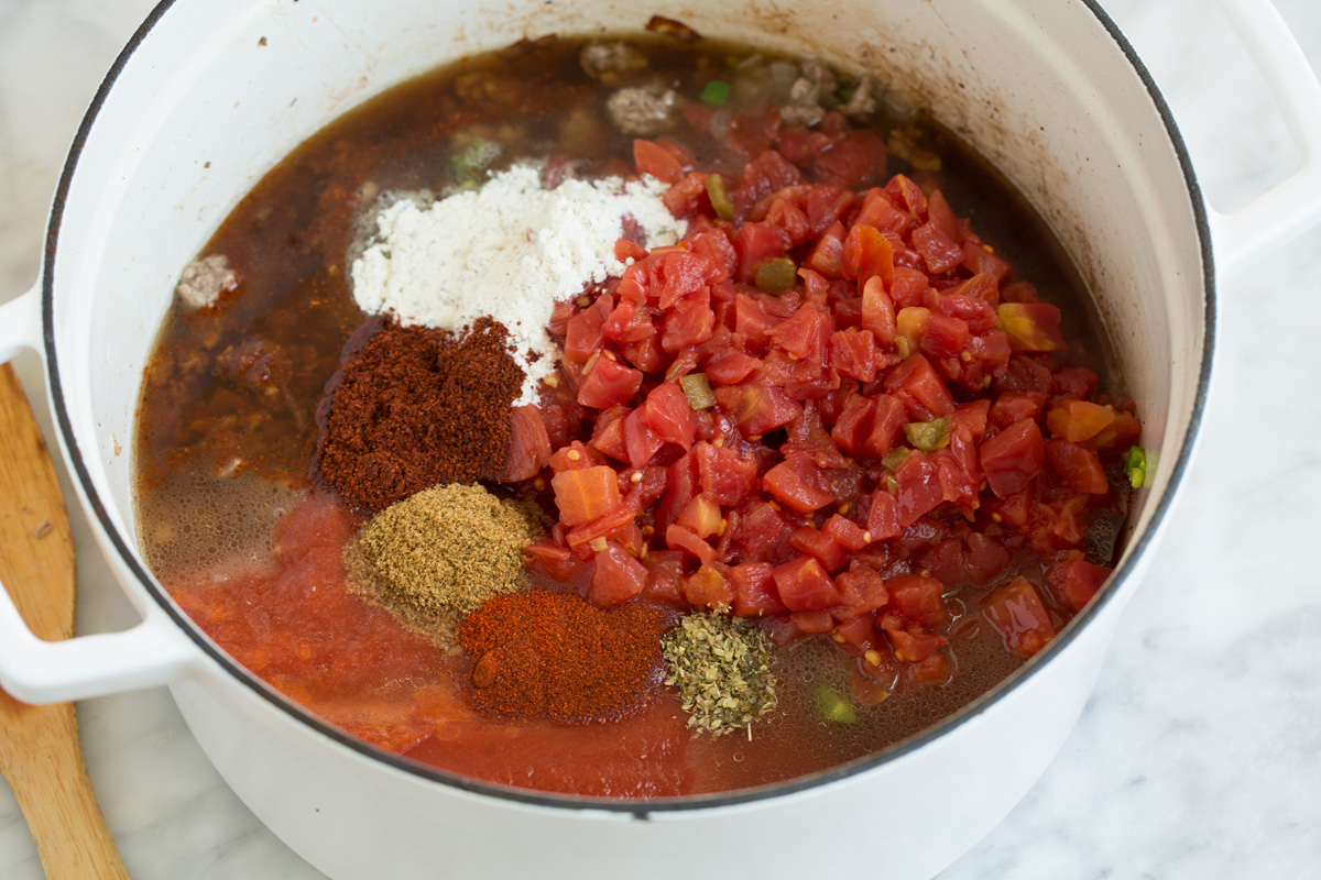Adding tomatoes and spices to pot to make taco soup.