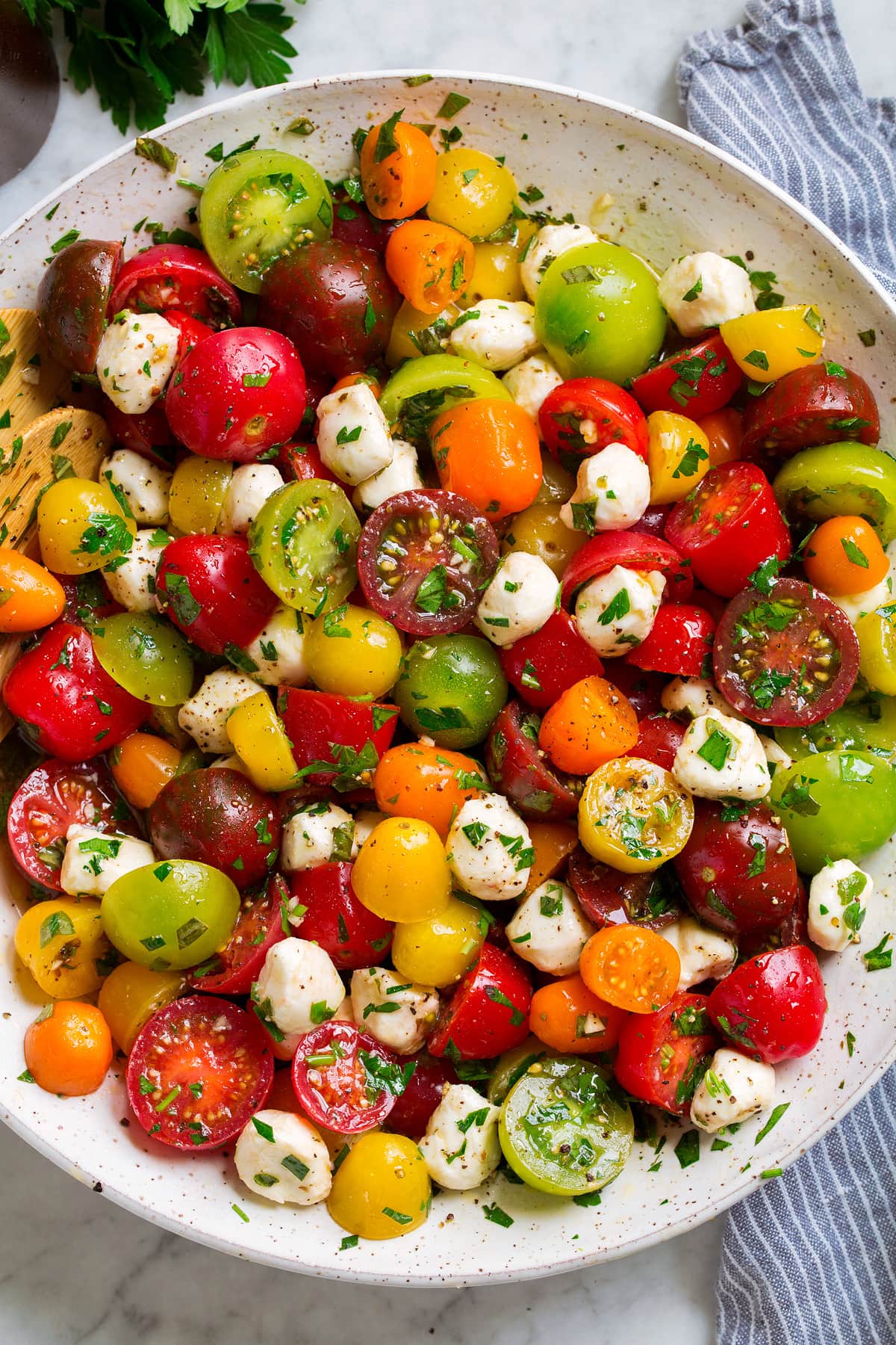 Tomato Salad in a white serving bowl. Shown in salad are multi-color cherry tomatoes and grape tomatoes, mozzarella pearls and it's coated in a herb dressing.