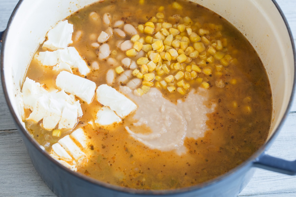 Adding cream cheese, corn and pureed bean mixture to white chicken chili mixture in pot.