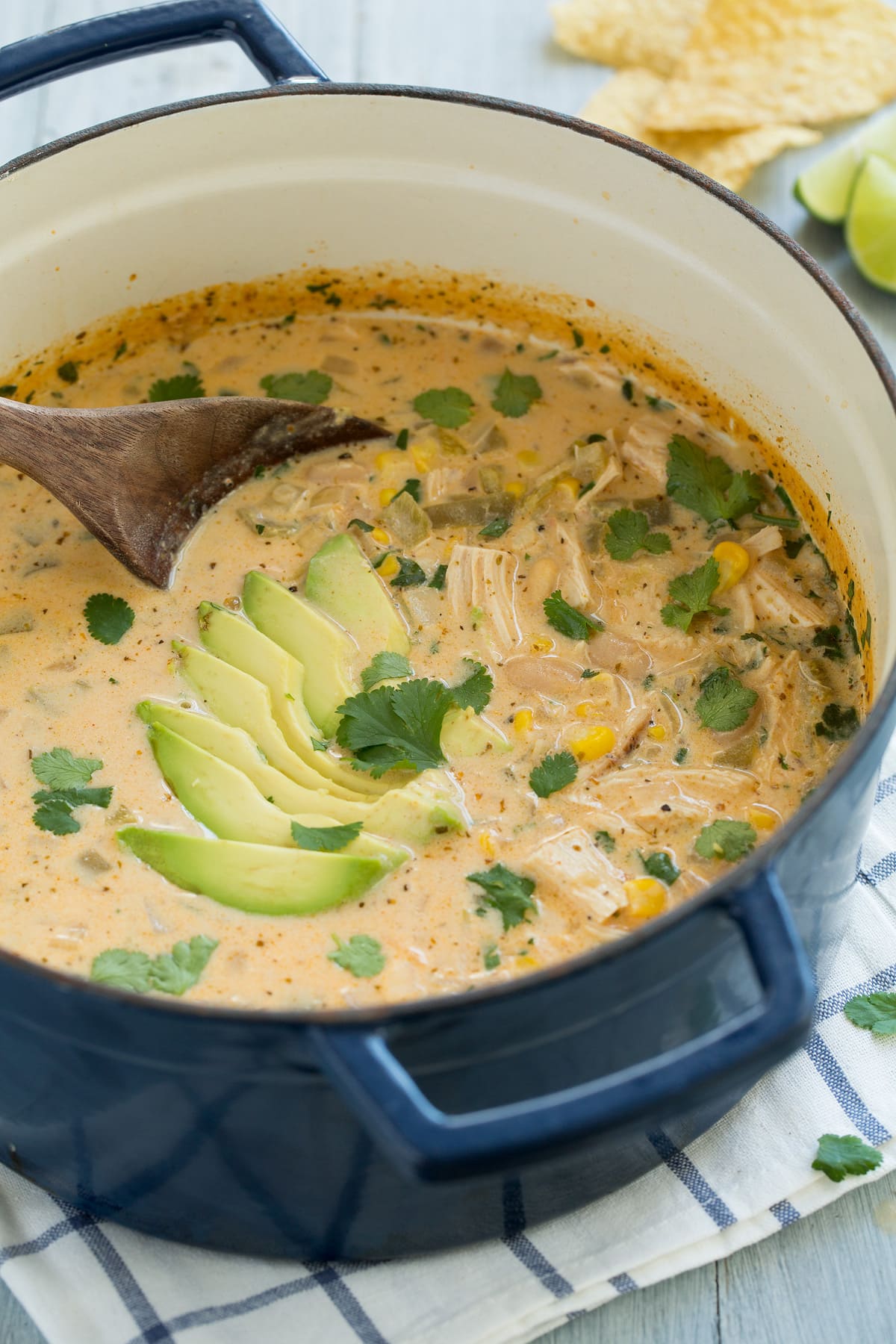 Navy blue pot full of white chicken chili. Chili includes pieces of chicken, pinto beans, corn, green chilies and a creamy broth, it is garnished with avocado and cilantro.