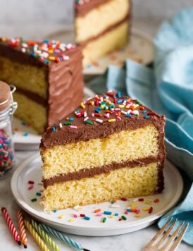 Slice of homemade yellow cake with chocolate frosting and sprinkles.