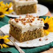 Two slices of homemade zucchini cake with cream cheese frosting with sunflowers decorating plates.